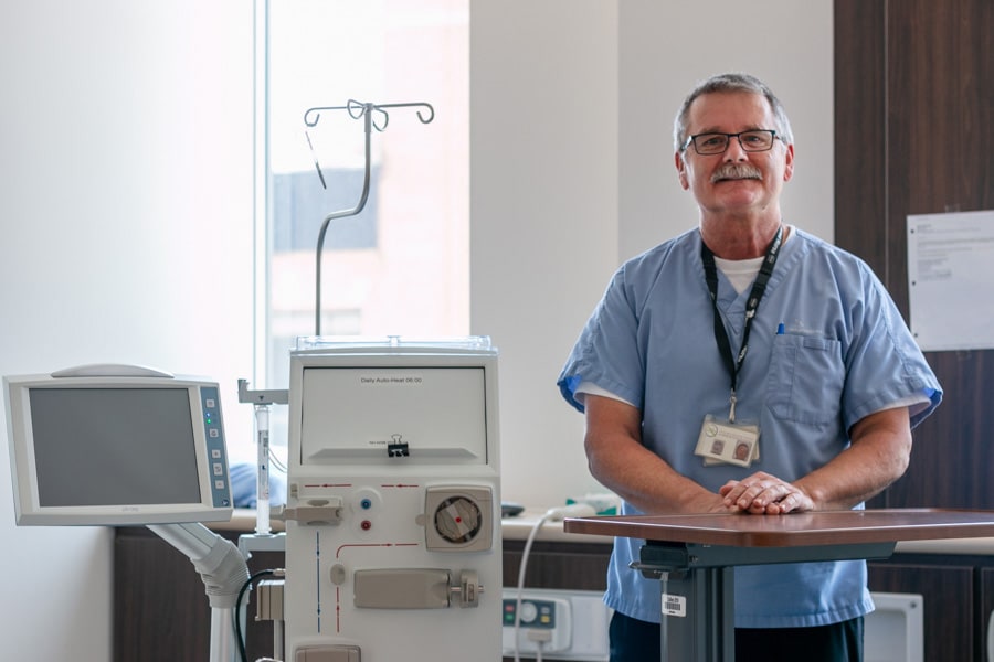 A man in medical scrubs stands next to a hemodialysis unit in a hospital