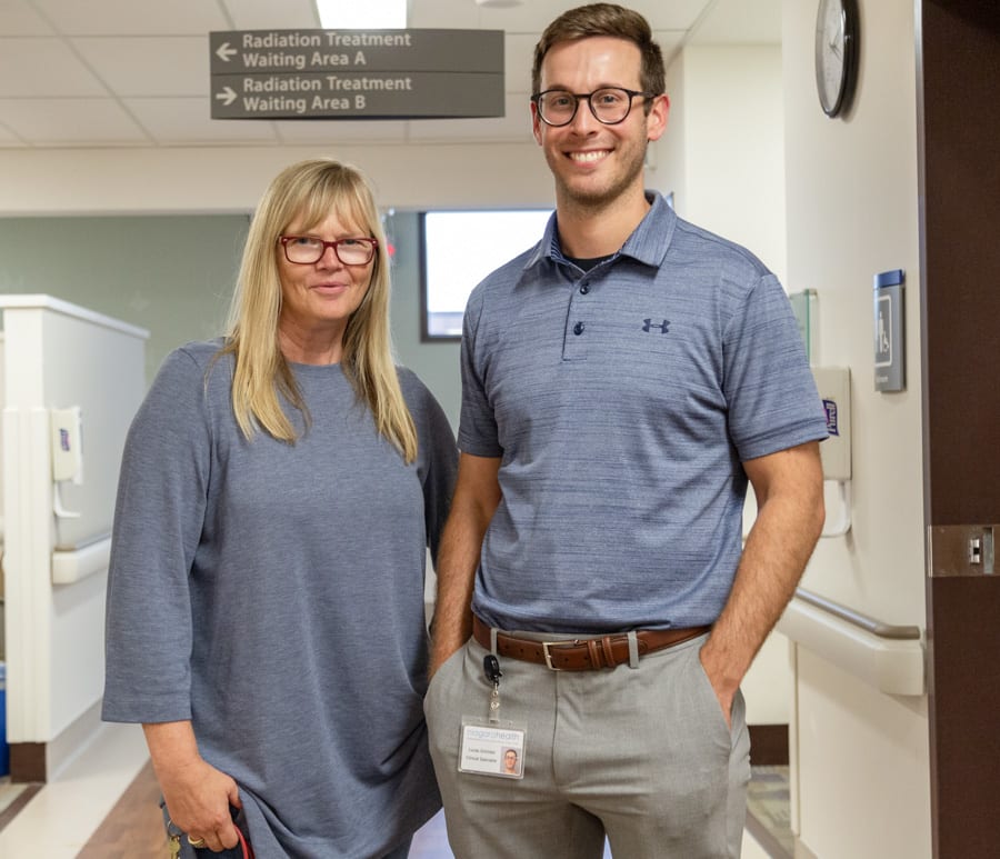 A woman with long blonde hair and a man wearing glasses stand near radiation bays in a hospital cancer centre.