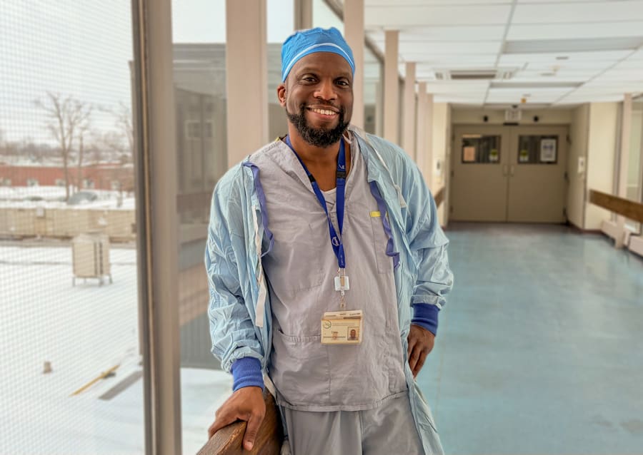Chris Domize is dressed in scrubs and stands in a windowed pedway at the Welland Hospital
