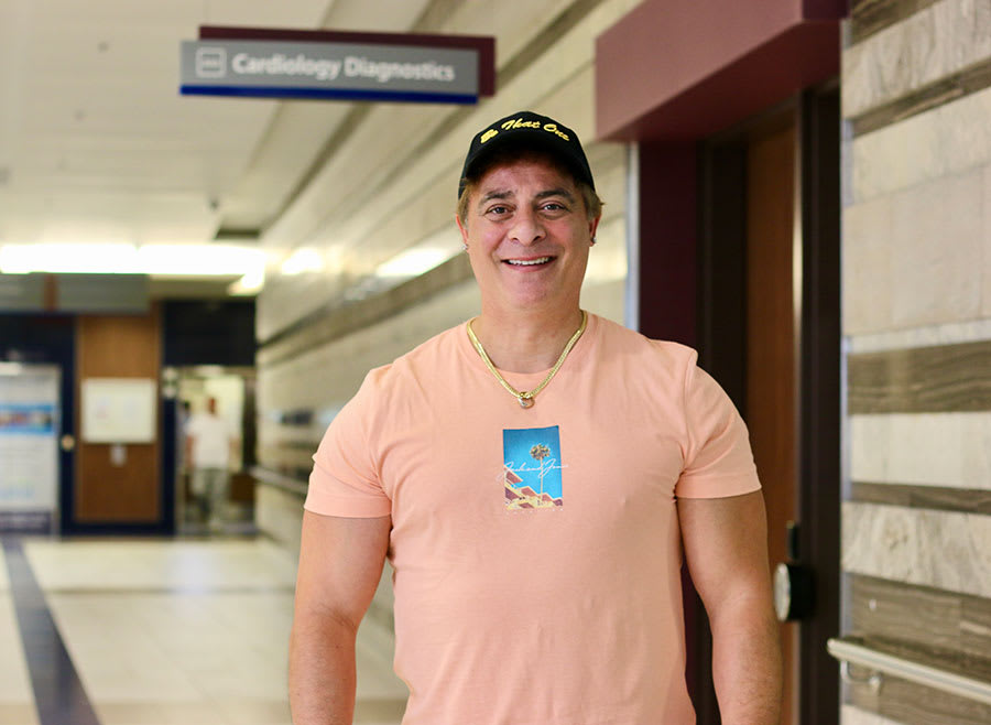 Former pro footballer Dan Giancola stands outside the cardiology program headquarters at the St. Catharines hospital. He is wearing a baseball cap and smiling for the camera.