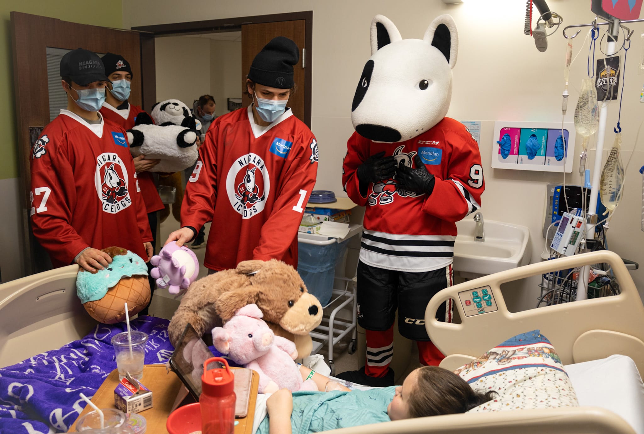 IceDogs players and mascot Bones deliver toys to a patient in a hospital bed