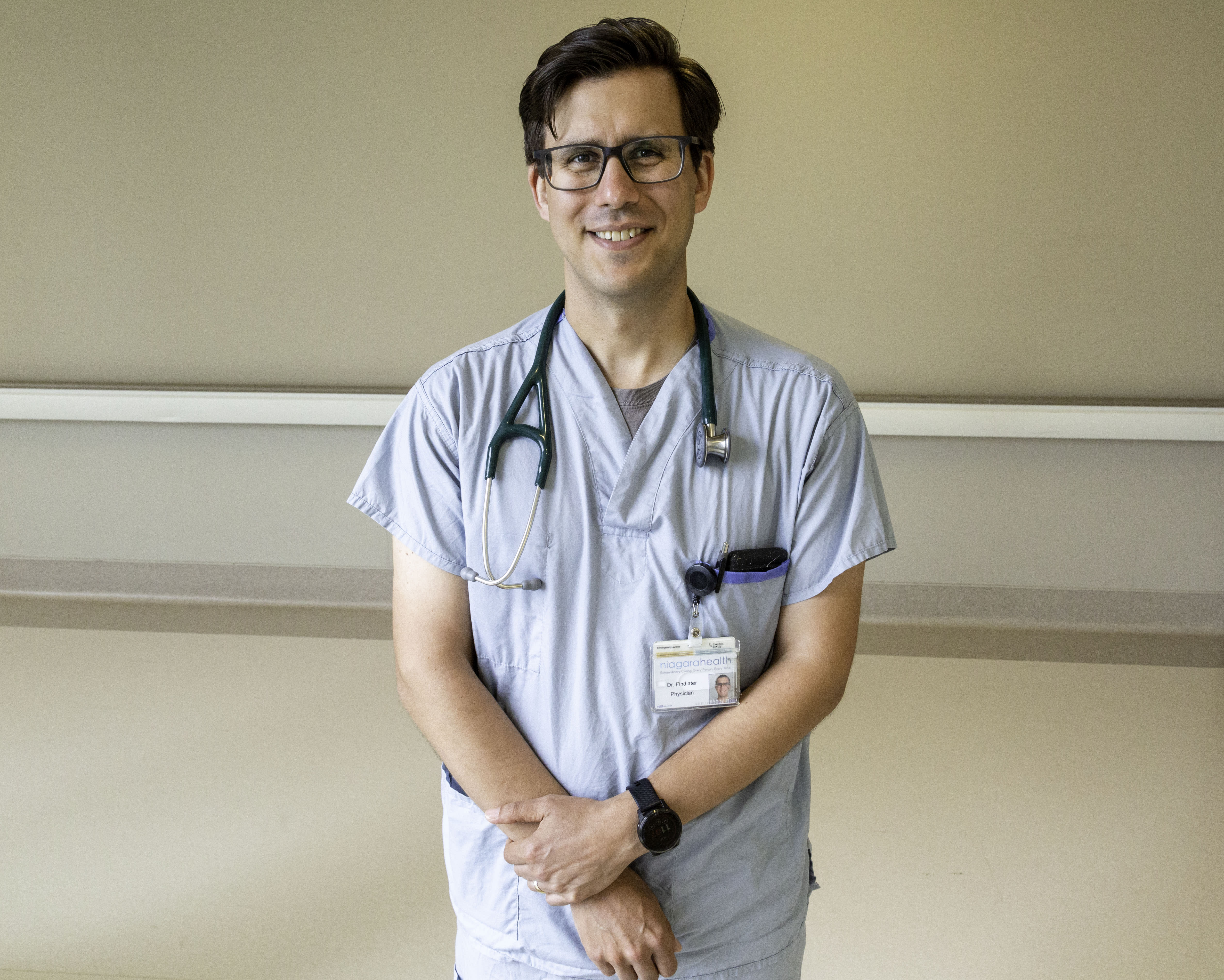 Dr. Aidan Findlater in scrubs, with a stethoscope around his neck in a hospital hallway.
