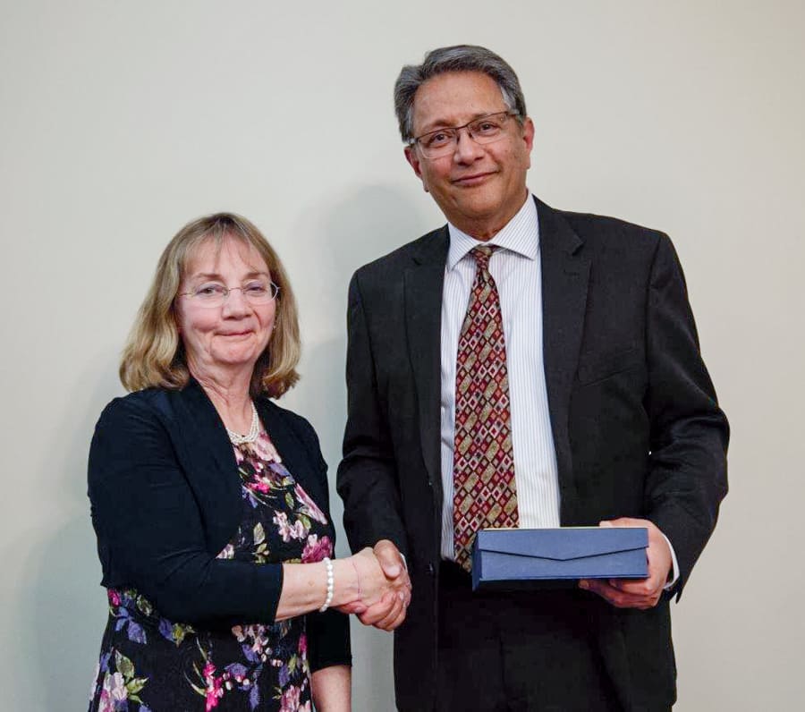 Two people stand together for a photo. One is presenting an award, the other receiving the award. 