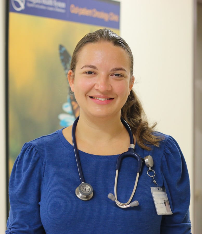 A young doctor wears a stethoscope around her neck and smiles for the camera