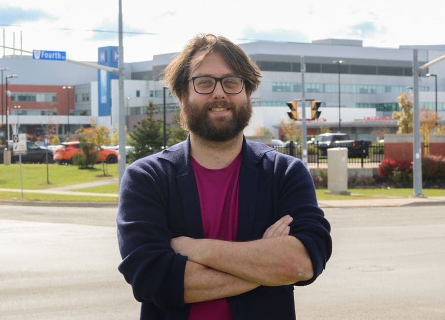 Dr. Stephenson Strobel stands outside the St. Catharines hospital. He is wearing glasses and a blue cardigan sweater. 