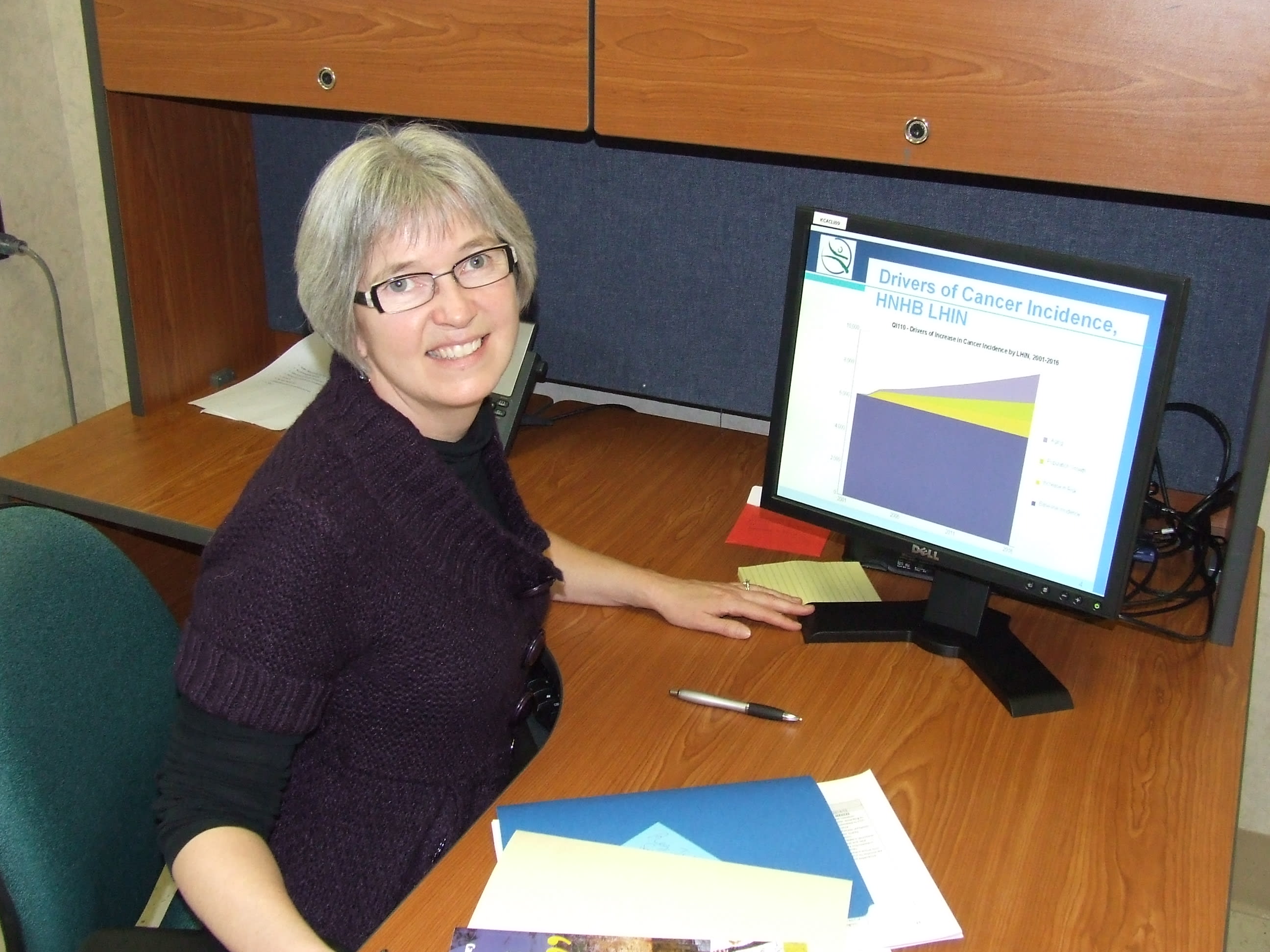A woman sits at her desk with a computer showing a incidence rate chart for cancer