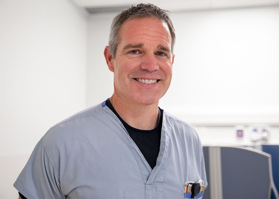 A doctor in scrubs smiles for the camera.