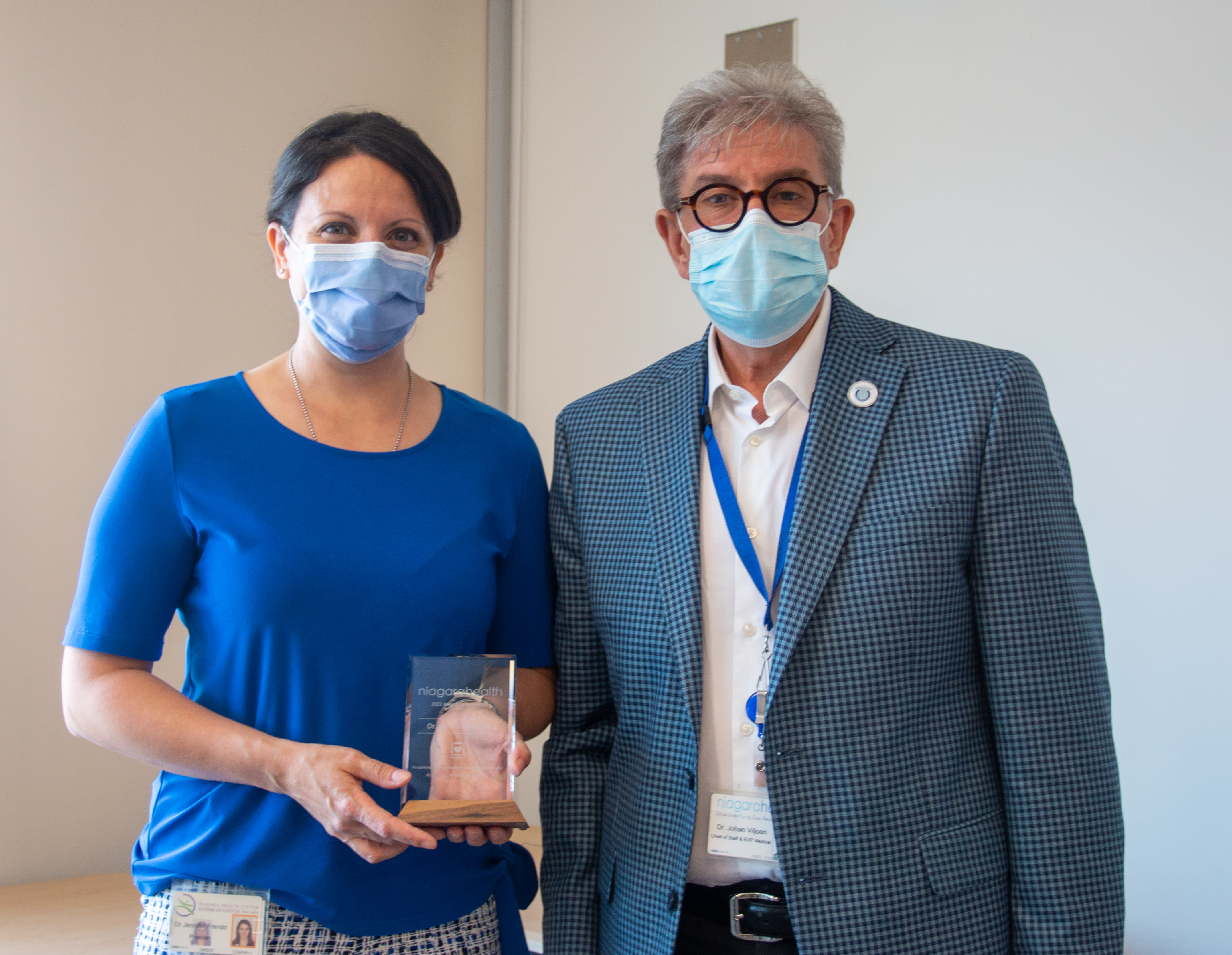 A man and woman stand together. The woman is holding an award.