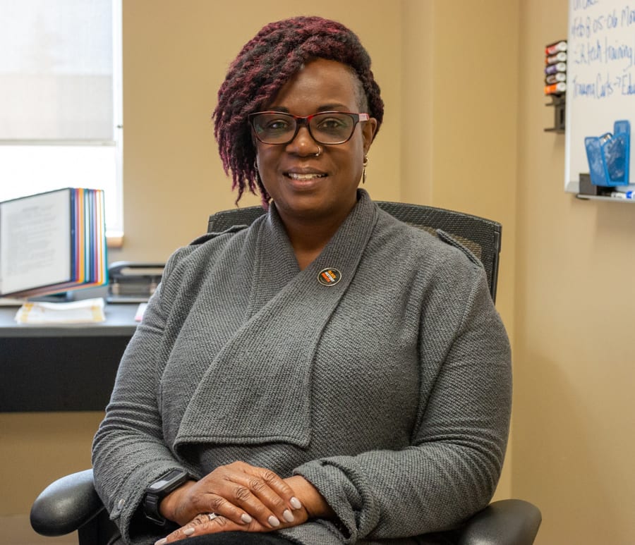 A Black woman wears a Black History Month pin and sits in her office at a hospital. She is smiling for the camera.