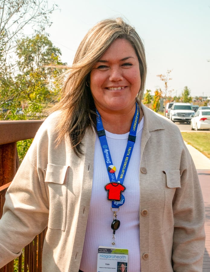 A woman stands outside on a bridge, smiling for the camera.