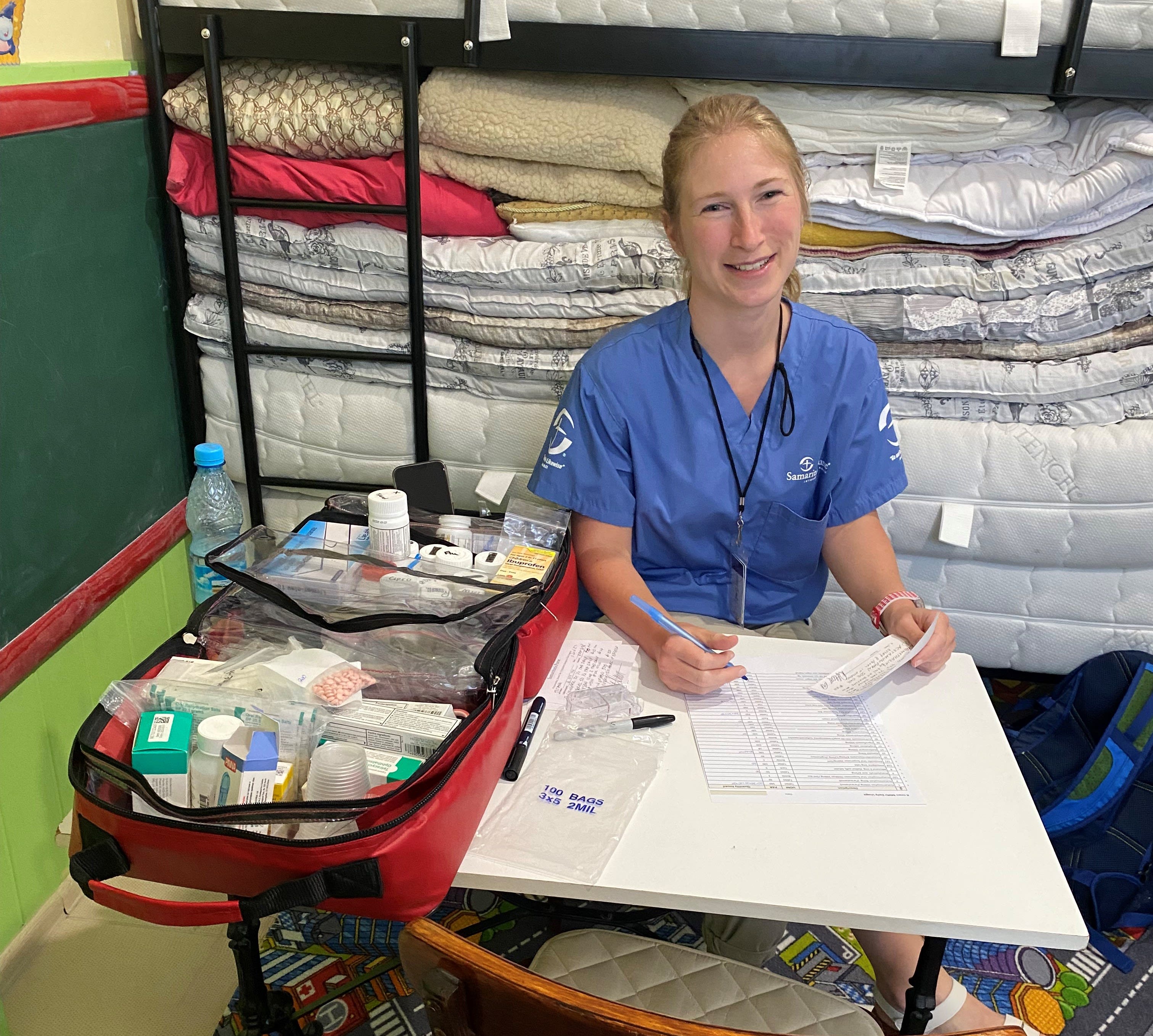 A woman with a bag of medicine does paperwork and smiles for the camera