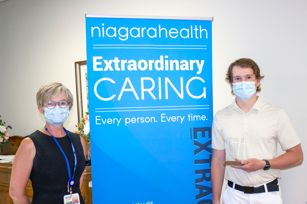 A man holding an award stands with a woman. They are wearing masks but smiling with their eyes.