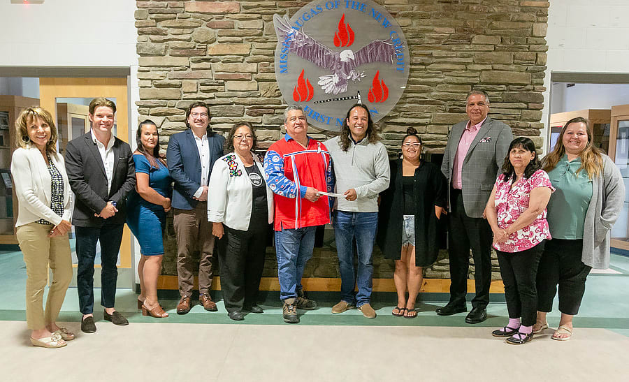 A group of people stand in front of the logo for the Mississaugas of the Credit First Nation