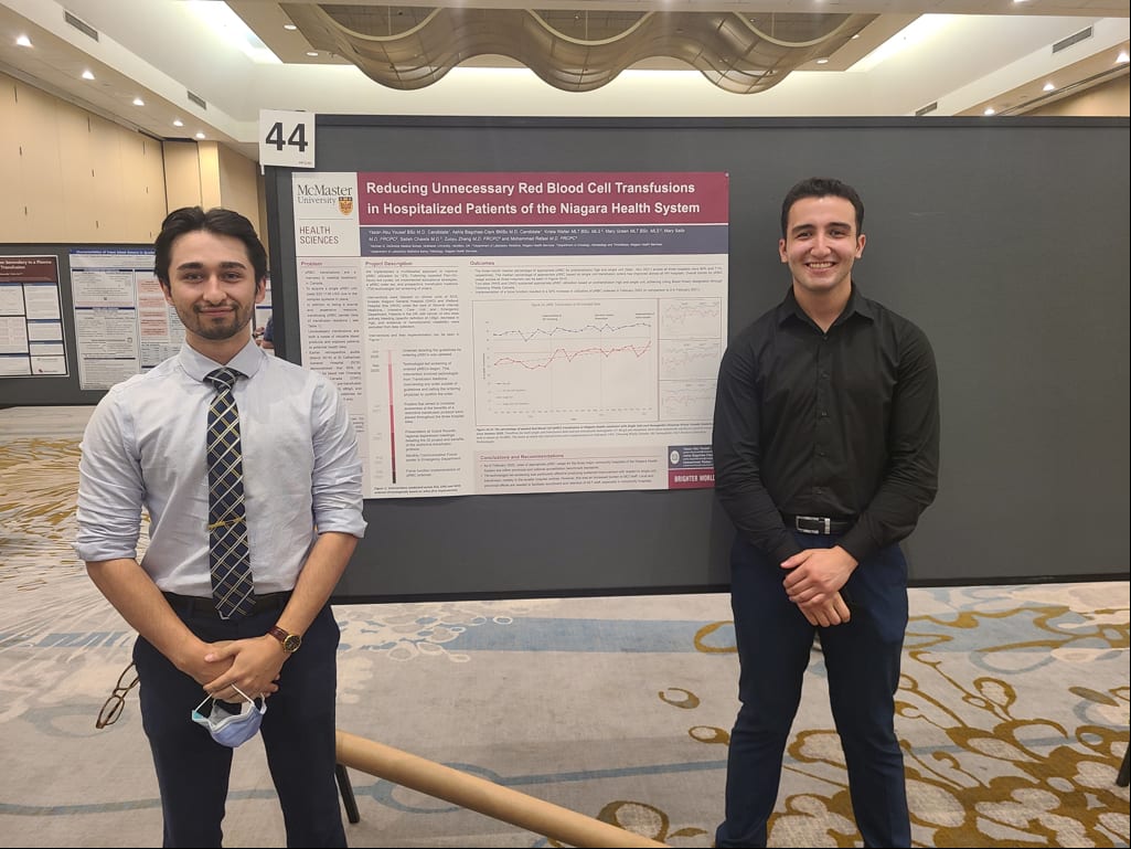 Two medical students stand in front of a poster about red blood cell transfusions.