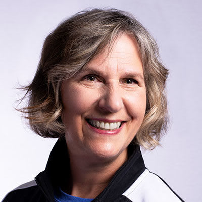 An older woman with wavy hair smiles at the camera.