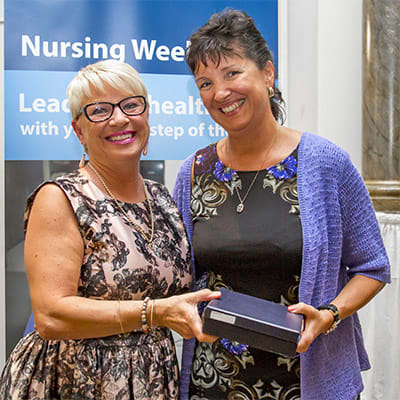 Two women smile for the camera is one is presented with an award.