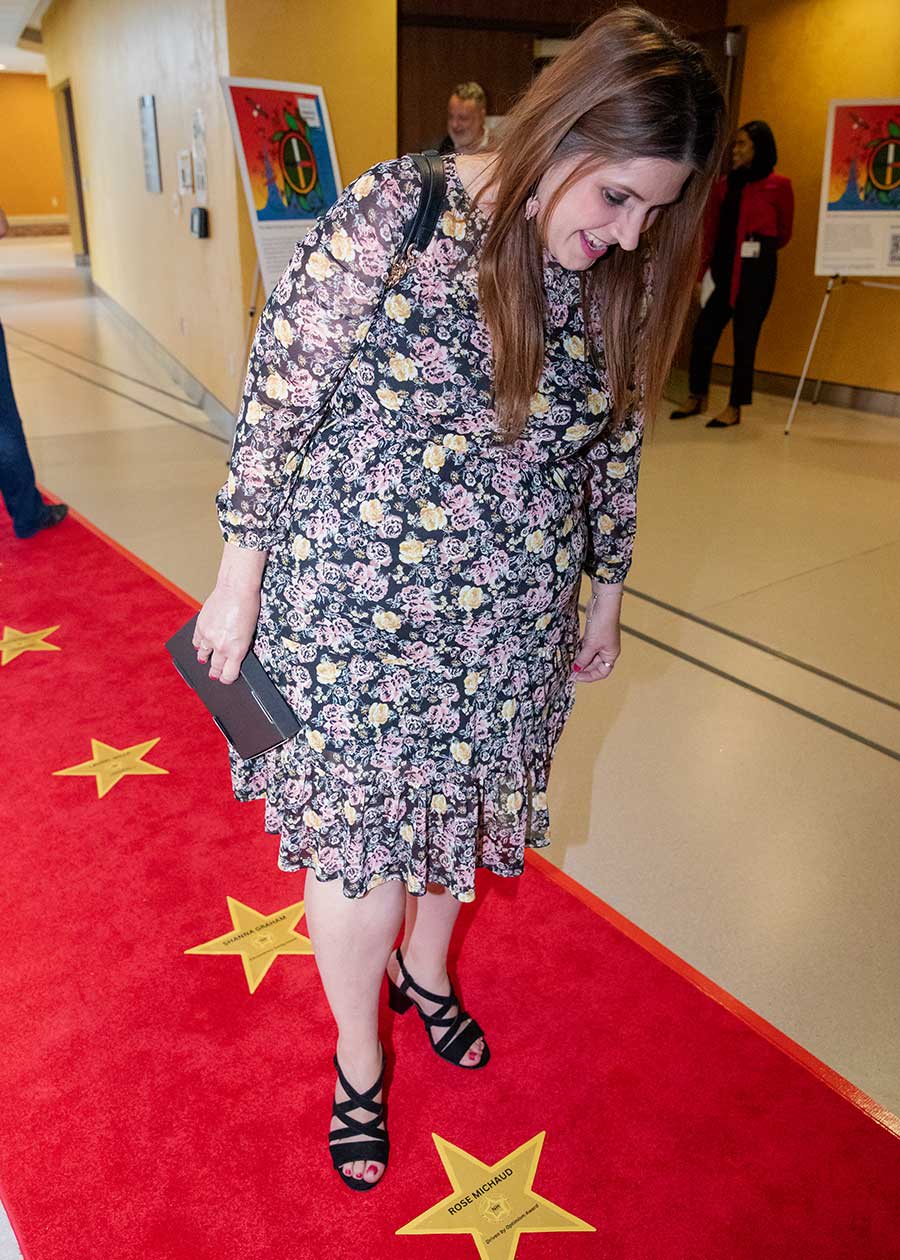 A woman with long hair and wearing a floral dress pauses to look at a star with her name written on it.