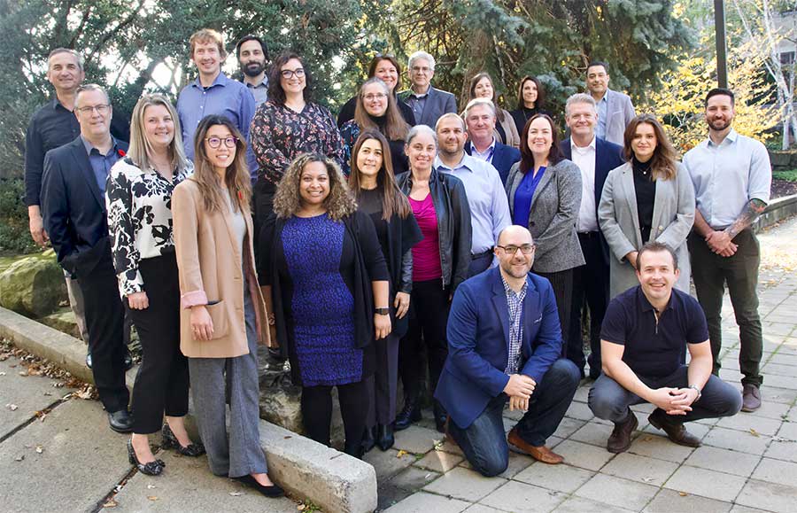 A large group of people gathered for a photo. They are standing outside with trees behind them. 