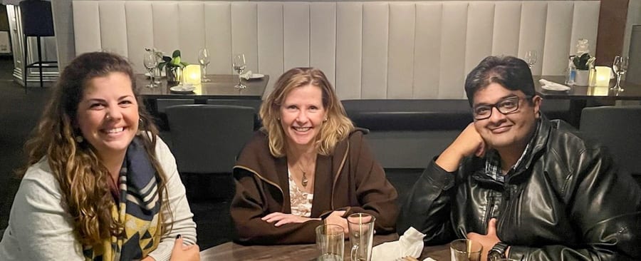 Three people sit around a table in a restaurant smiling for the camera