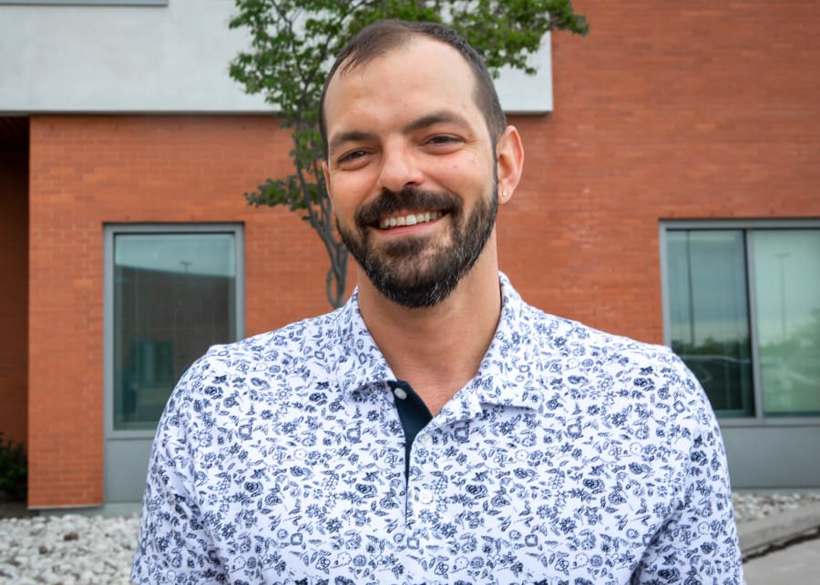 A man with a beard in a patterned blue and white shirt smiles for the camera 