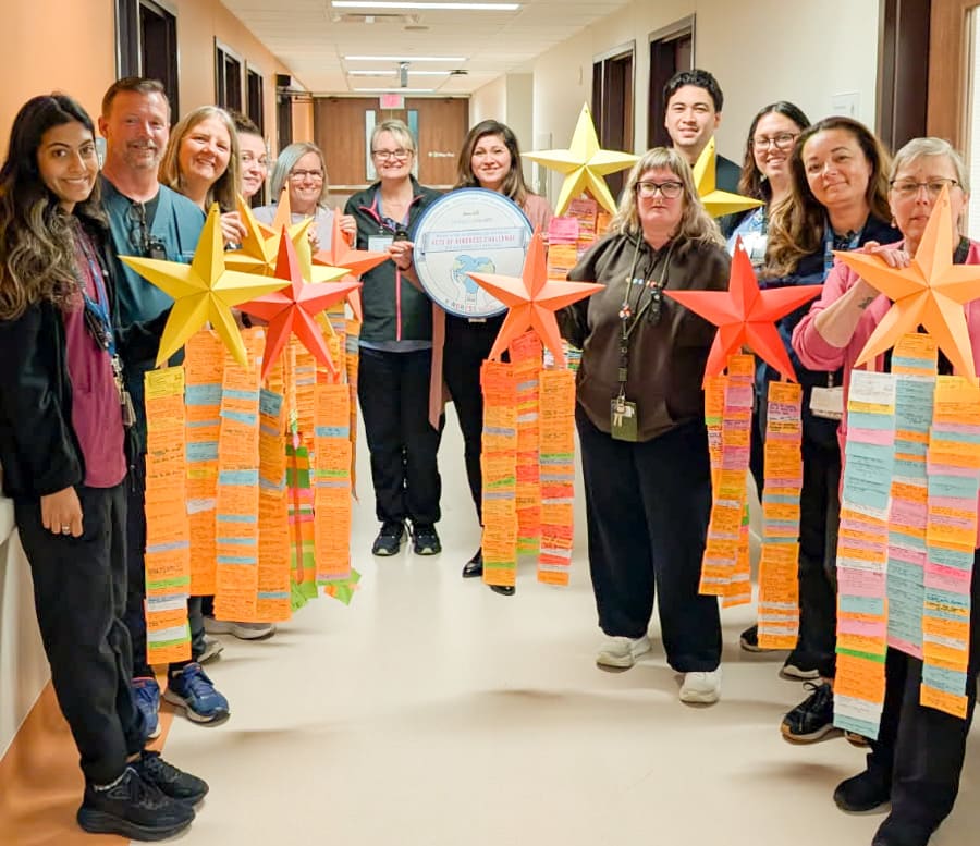 The team on Unit 1A holds up colourful paper stars with long streamers of post-it notes listing random acts of kindness.