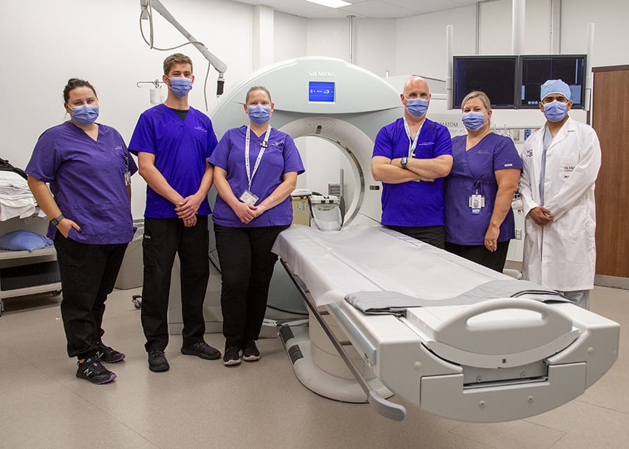 A group of clinicians stands around a CT scan machine