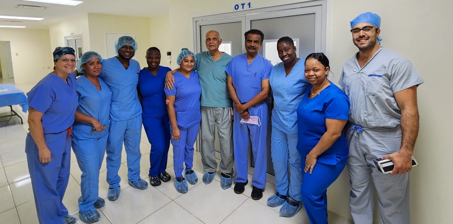 A large group of people stand in a hospital hallway. They are wearing scrubs